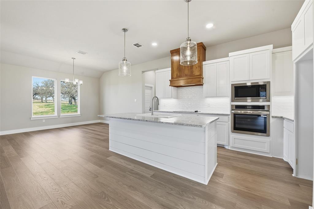 1973 Johnnie Drive Springtown, TX 76082 - Photo 11 of 38 Kitchen featuring decorative light fixtures, white cabinetry, stainless steel appliances, light stone counters, and an island with sink