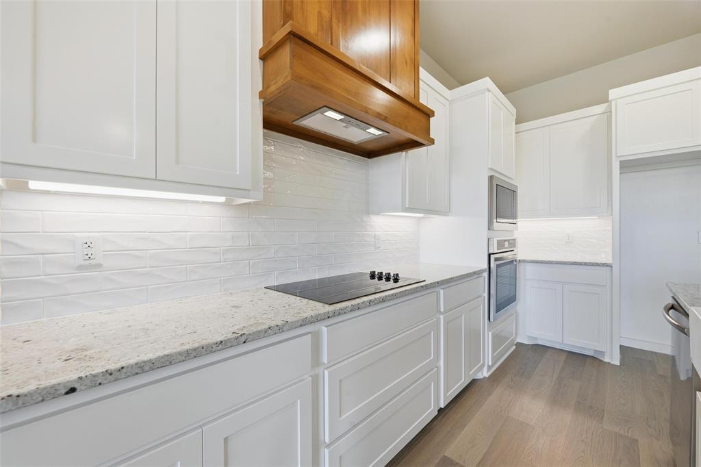 1973 Johnnie Drive Springtown, TX 76082 - Photo 15 of 38 Kitchen featuring white cabinets, light wood-style floors, light stone countertops, decorative backsplash, and stainless steel appliances