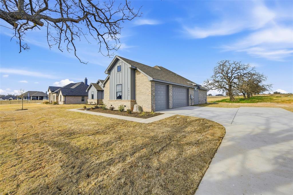1973 Johnnie Drive Springtown, TX 76082 - Photo 3 of 38 View of home's exterior with board and batten siding, brick siding, driveway, a yard, and an attached garage