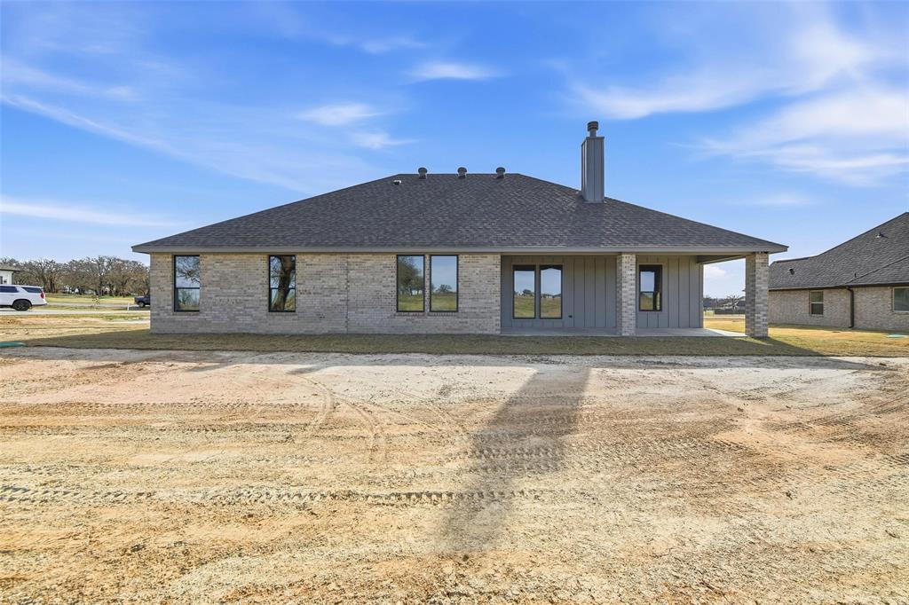 1973 Johnnie Drive Springtown, TX 76082 - Photo 36 of 38 Back of property with board and batten siding, a patio, a chimney, roof with shingles, and brick siding