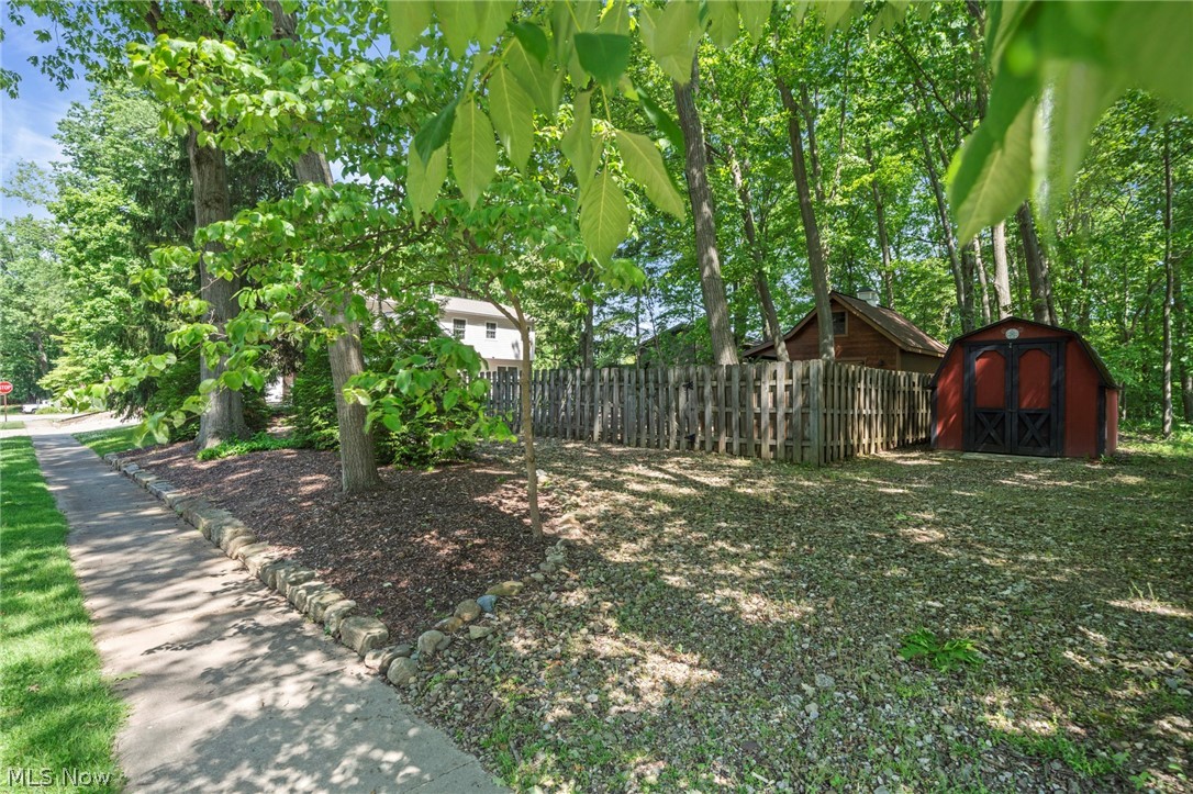 3871 Greentree Road Stow, OH 44224 - Photo 44 of 50 Expansive treed lot featuring a sidewalk, stone border landscaping, a privacy fence, and a red storage shed
