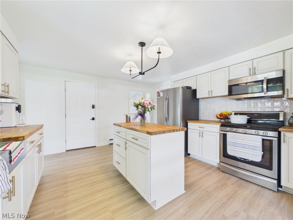 3490 County Line Road Madison, OH 44057 - Photo 21 of 42 Kitchen featuring an island with wood-finish countertop, stainless steel appliances, white cabinetry with gold-tone hardware, a tiled backsplash, and wood-finish flooring