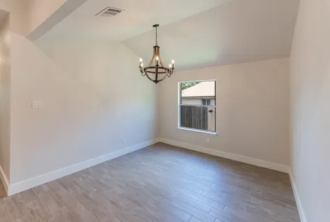an empty room with wooden floor chandelier and windows