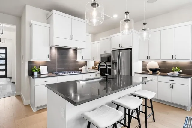 a kitchen with a refrigerator a sink dishwasher a stove a dining table and chairs with wooden floor