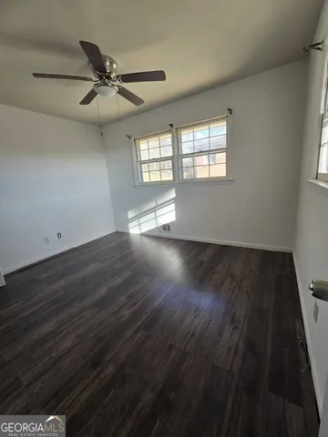 an empty room with wooden floor fan and windows