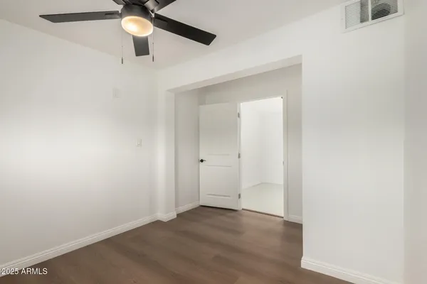 an empty room with a chandelier fan and wooden floor