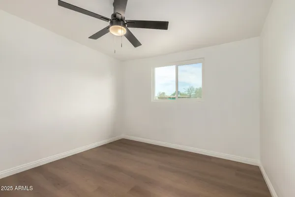 an empty room with wooden floor ceiling fan and window