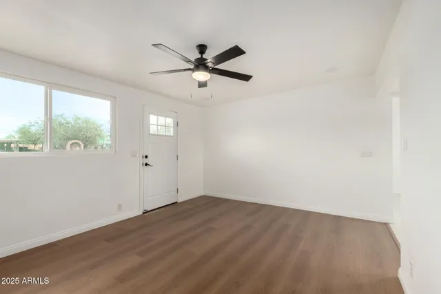 an empty room with wooden floor fan and windows