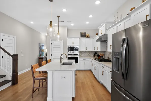 a kitchen with stainless steel appliances kitchen island granite countertop a refrigerator a stove top oven a sink dishwasher and white cabinets with wooden floor