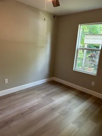 a view of an empty room with wooden floor and a window