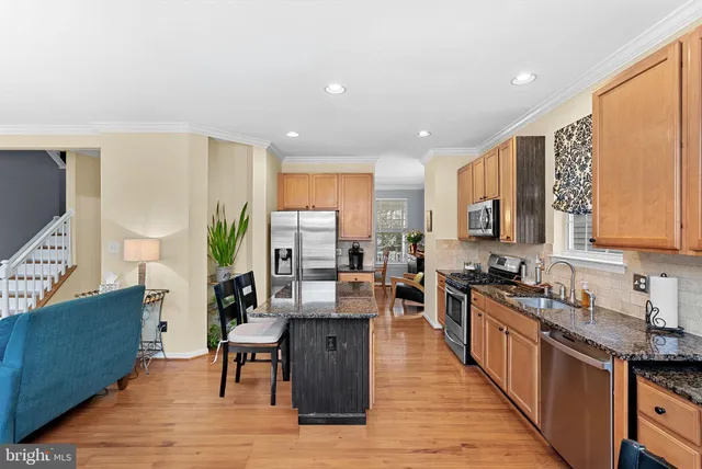 a living room with stainless steel appliances granite countertop a kitchen island a stove a refrigerator a couch and a dining table with wooden floor