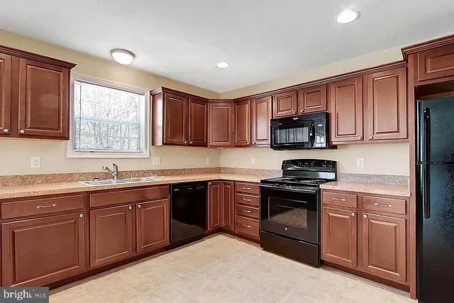 a kitchen with stainless steel appliances granite countertop wooden cabinets a sink a stove a refrigerator with grey cabinets and a window