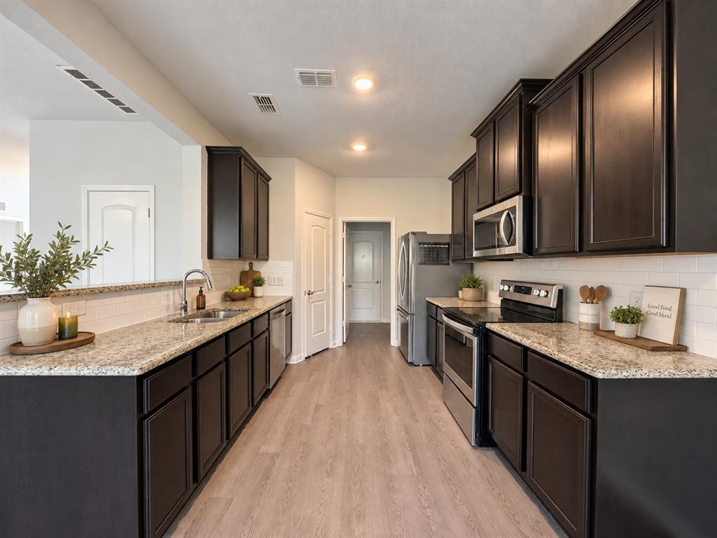 2950 Parker Road Anna, TX 75409 - Photo 4 of 12 Wood-finish flooring, dark wood cabinetry, light-toned countertops, white subway tile backsplash, and stainless steel appliances
