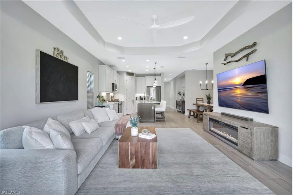 4621 Centaurus Circle Naples, FL 34120 - Photo 4 of 47 Living room with wood tiled floors, a glass covered fireplace, a tray ceiling, ceiling fan, and recessed lighting staged for photo