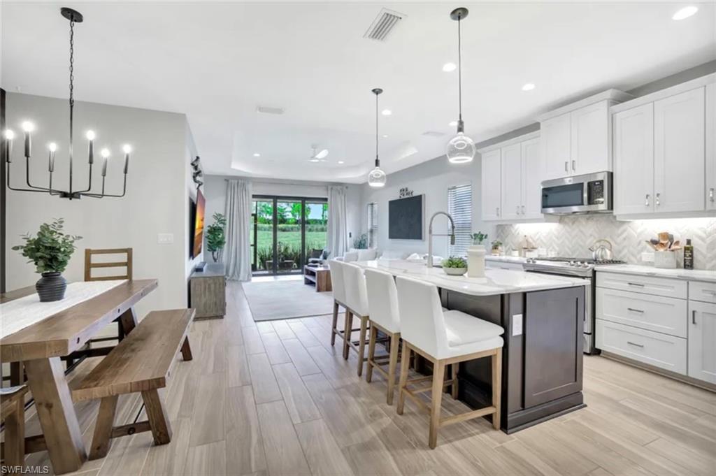4621 Centaurus Circle Naples, FL 34120 - Photo 7 of 47 Kitchen with white cabinetry, stainless steel appliances, a kitchen island with sink, light stone countertops, and recessed lighting staged for photo