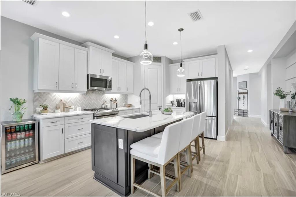 4621 Centaurus Circle Naples, FL 34120 - Photo 7 of 47 Kitchen featuring appliances with stainless steel finishes, a kitchen bar, white cabinets, and hanging light fixtures staged for photo