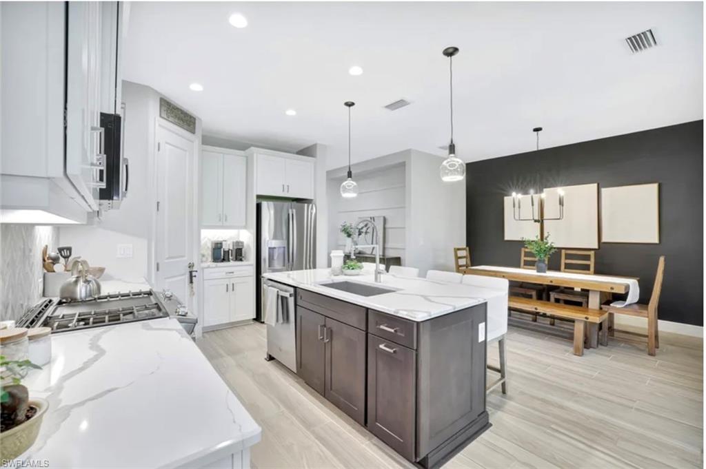 4621 Centaurus Circle Naples, FL 34120 - Photo 8 of 47 Kitchen featuring decorative light fixtures, light stone counters, white cabinets, a kitchen island with sink, and recessed lighting staged for photo