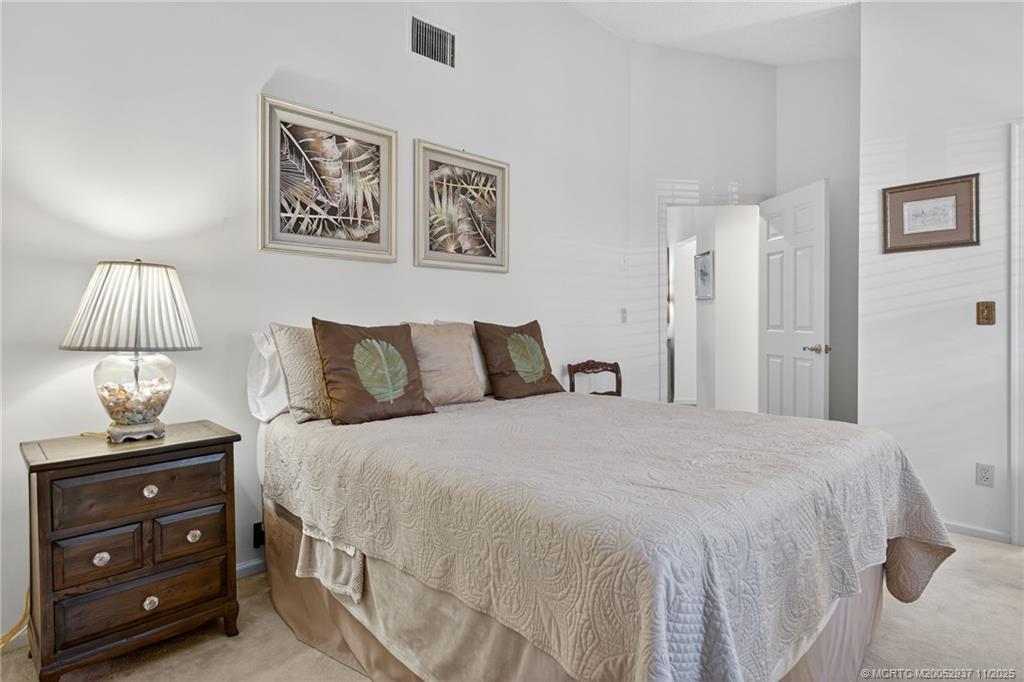 6001 Southeast Martinique Drive, Unit 104 Stuart, FL 34997 - Photo 27 of 36 a bedroom with a bed and a lamp on table