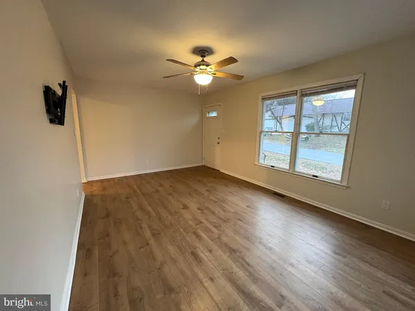 an empty room with wooden floor fan and windows