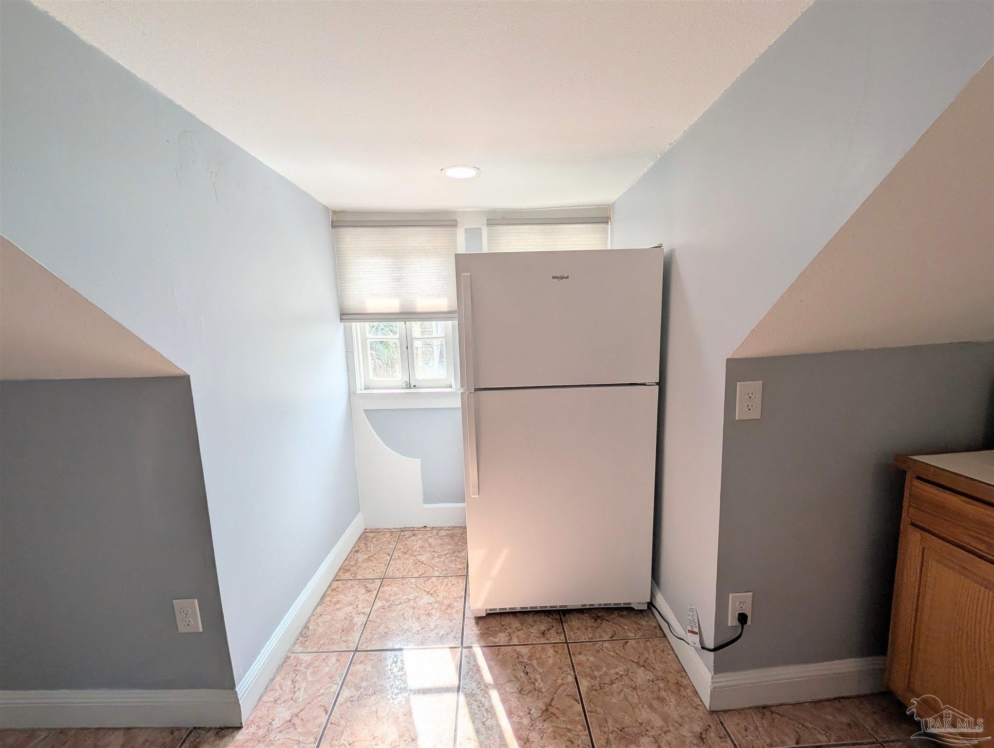 911 North Spring Street, Unit 4 Pensacola, FL 32501 - Photo 10 of 16 a view of a refrigerator in kitchen and an empty room with wooden floor