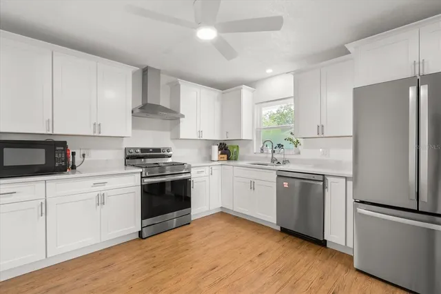 a kitchen with stainless steel appliances granite countertop white cabinets a refrigerator a sink a stove a microwave and wooden floors