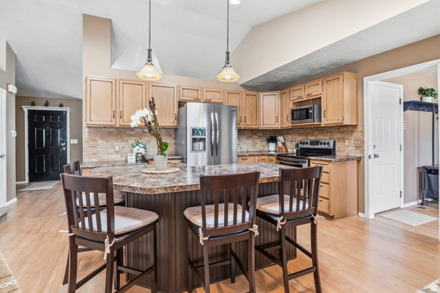 1101 Old Dairy Road Sandy, UT 84094 - Photo 10 of 36 Kitchen featuring an angled breakfast bar with pendant lighting, light wood-finish cabinetry, stainless steel appliances, a tile backsplash, and wood-finish flooring