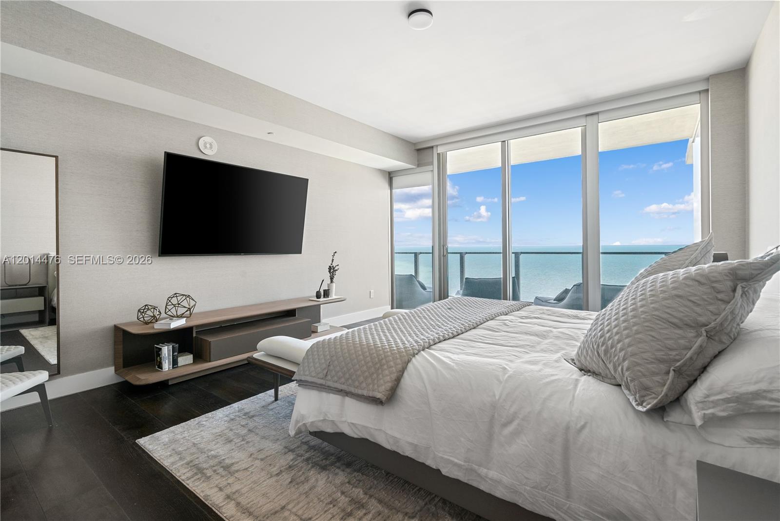 360 Ocean Drive, Unit 1106S Key Biscayne, FL 33149 - Photo 23 of 67 Primary Bedroom – The primary bedroom captures direct water views through floor-to-ceiling glass doors that open to the balcony. A wall-mounted TV, sleek media console, and layered neutral textures create a calm retreat.