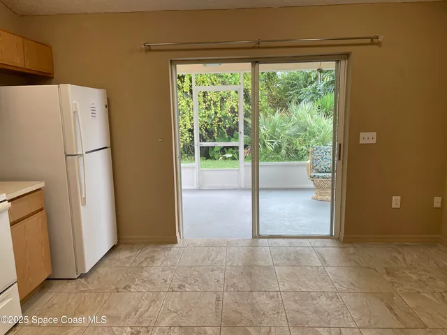 a view of an empty room with a kitchen view and a refrigerator