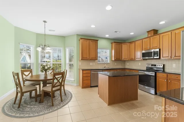a kitchen with stainless steel appliances granite countertop a stove top oven a sink a dining table and chairs