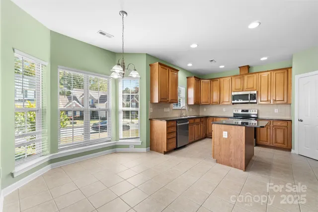 a kitchen with stainless steel appliances granite countertop a stove top oven a sink dishwasher a dining table and chairs a refrigerator with wooden floor