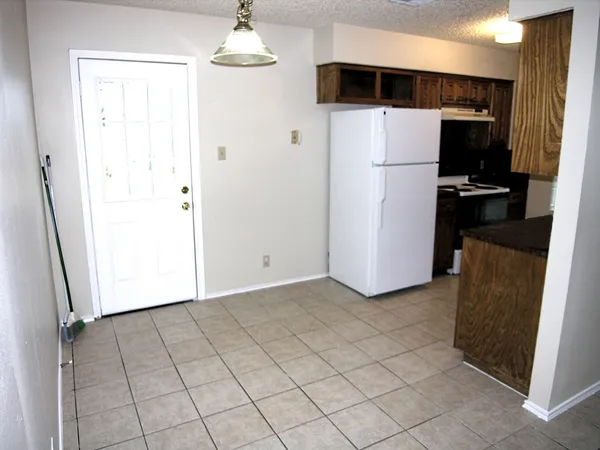 a view of a refrigerator in kitchen and an empty room with wooden floor