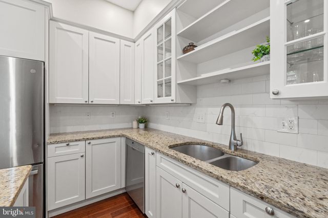 a kitchen with stainless steel appliances granite countertop a sink a refrigerator and white cabinets
