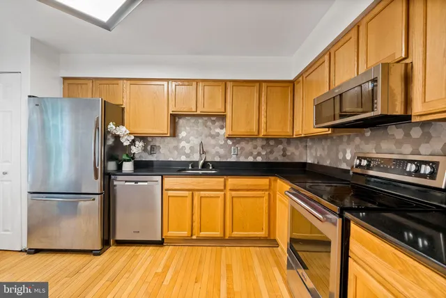 a kitchen with stainless steel appliances granite countertop a refrigerator a sink dishwasher a stove and white countertops with wooden floor