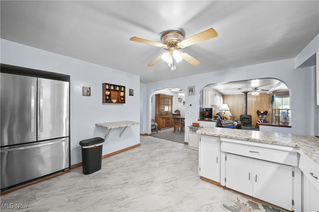6677 Fee Road Rome, OH 44085 - Photo 12 of 39 Kitchen featuring a wood stove, ceiling fan, stainless steel refrigerator, and white cabinets