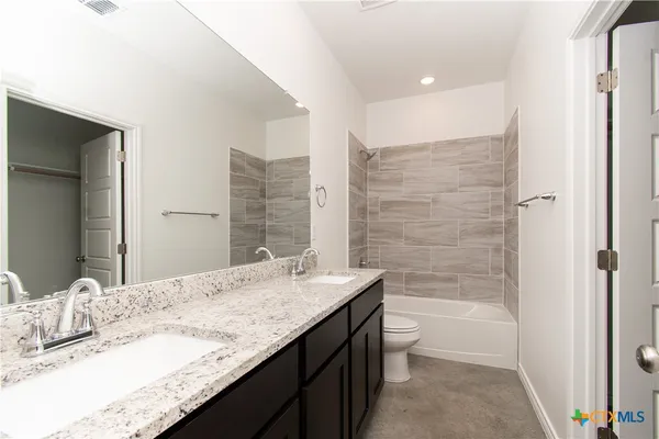a bathroom with a granite countertop bathtub sink vanity mirror and toilet
