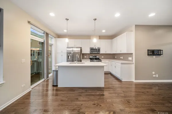 a large white kitchen with a refrigerator a kitchen island a stove and a wooden floor