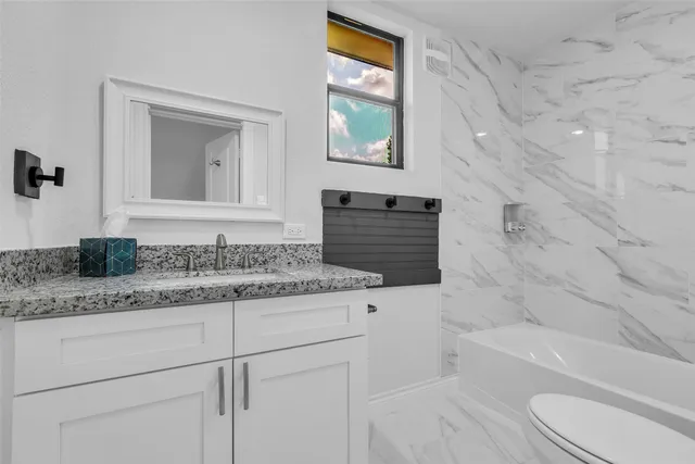 a bathroom with a granite countertop sink toilet vanity mirror bathtub and shower