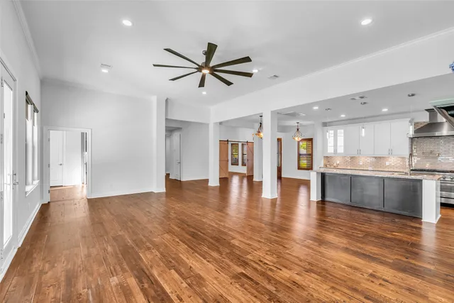 a view of an empty room and kitchen with wooden floor
