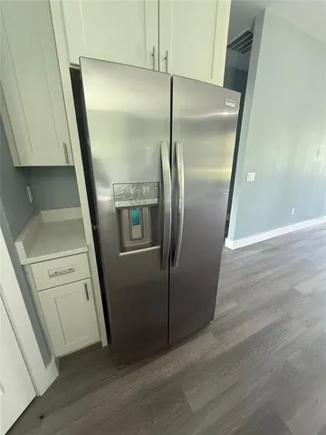 a view of a refrigerator in kitchen and an empty room with wooden floor