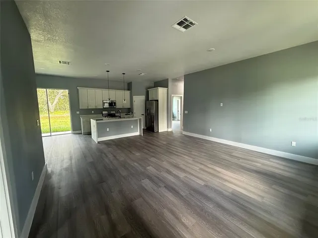 an empty room with wooden floor kitchen view and a window