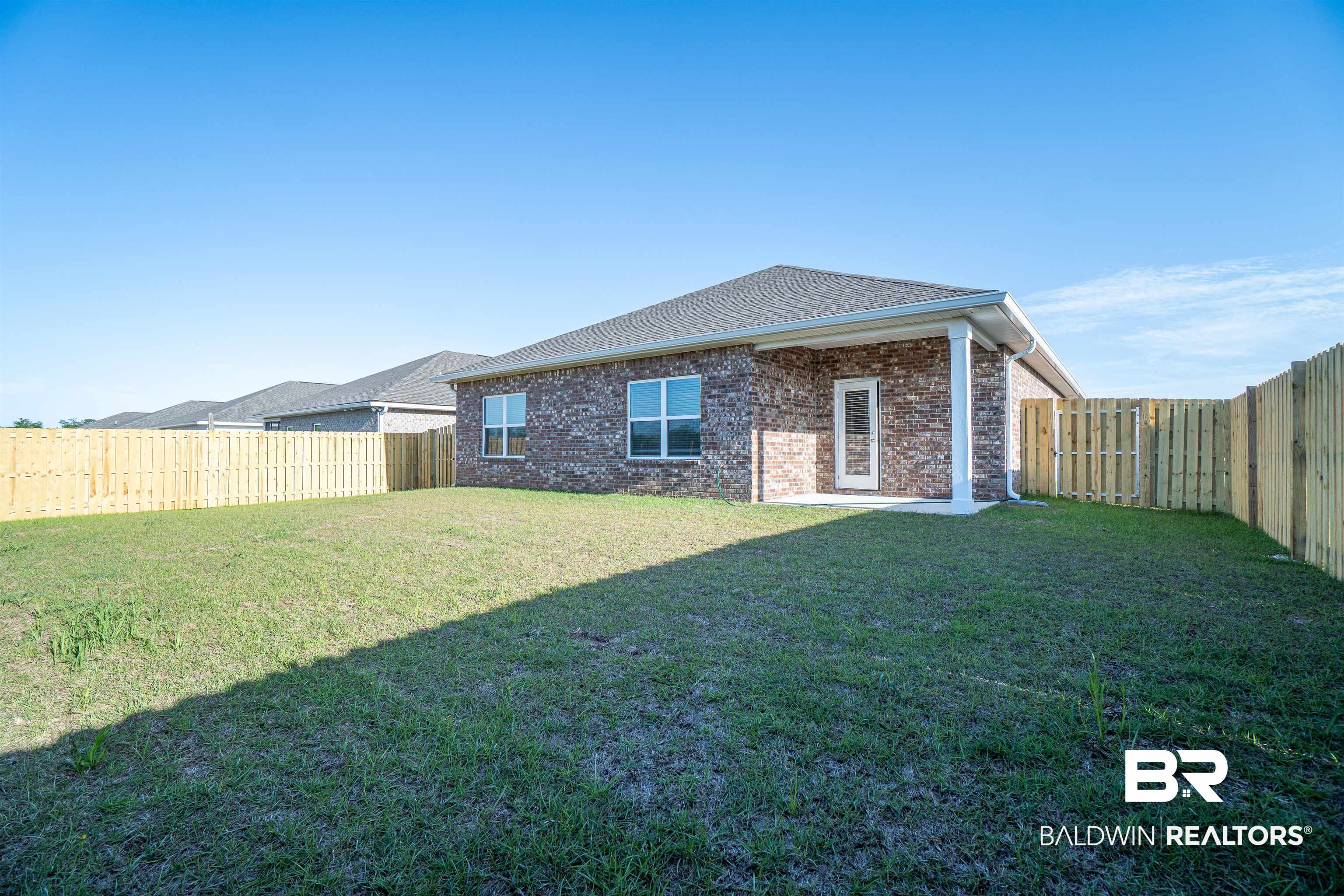 1073 Hayward Loop Foley, AL 36535 - Photo 3 of 18 Spacious fenced backyard with a grass lawn, brick exterior, covered patio, and privacy fencing