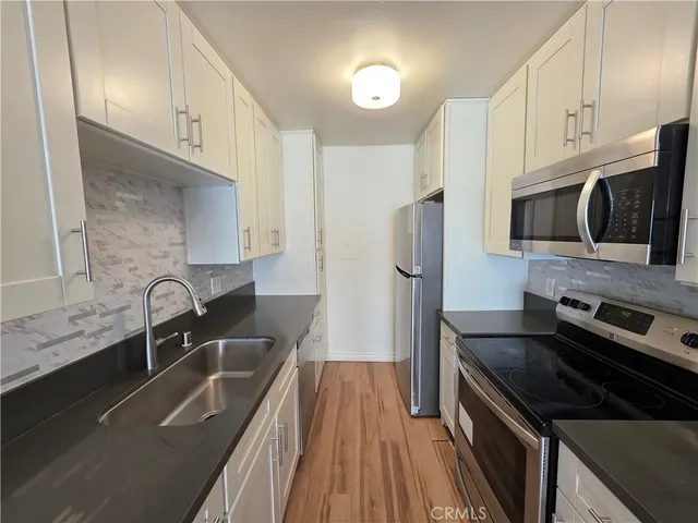 a kitchen with granite countertop a sink dishwasher stove and refrigerator with wooden floor