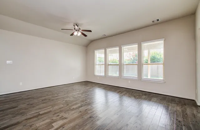 an empty room with wooden floor ceiling fan and windows