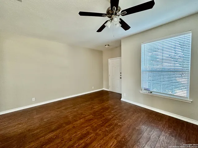 an empty room with wooden floor fan and windows