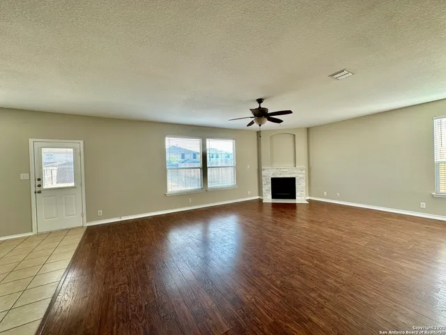 an empty room with wooden floor fireplace and windows