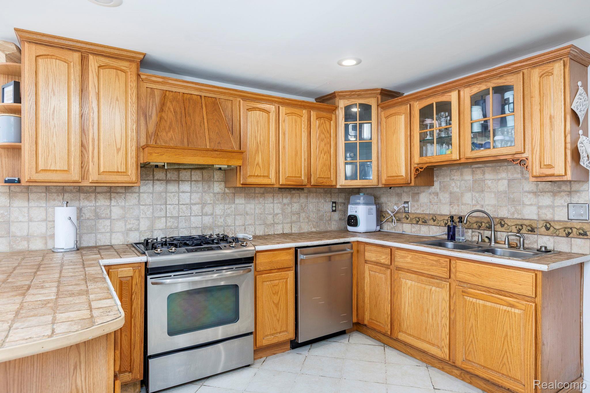 401 Pointe Tremble Road Algonac, MI 48001 - Photo 18 of 40 Kitchen featuring extensive wood cabinetry, stainless steel oven with gas cooktop, stainless steel dishwasher, tile countertops, and a full tile backsplash