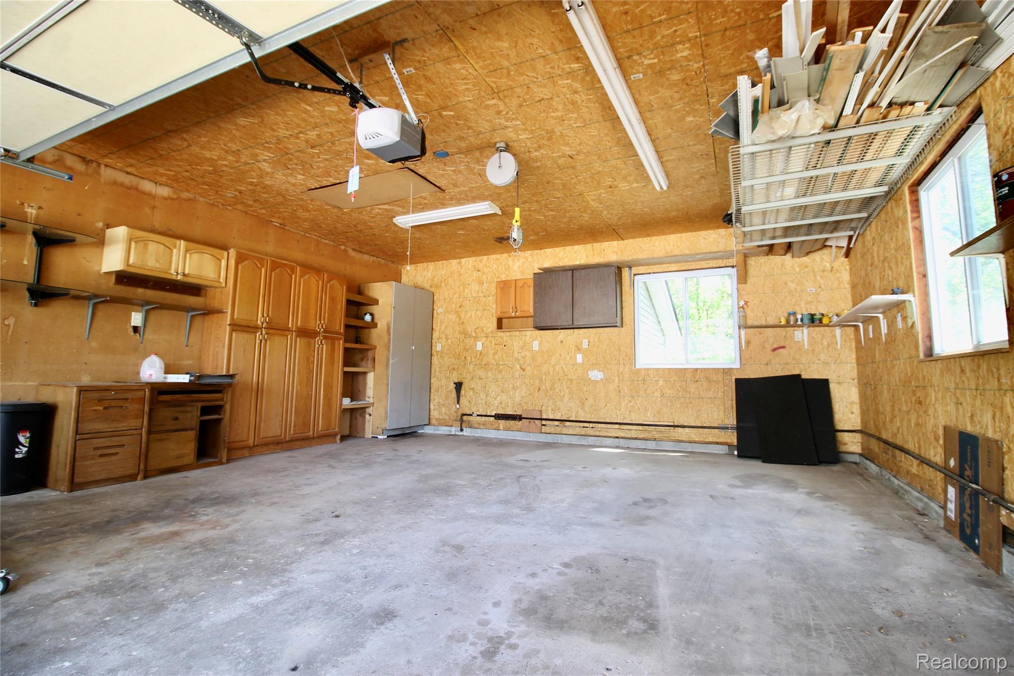 8372 Parshallville Road Fenton, MI 48430 - Photo 32 of 44 Spacious garage featuring a concrete floor, plywood walls, built-in cabinetry, overhead fluorescent lighting, and multiple windows