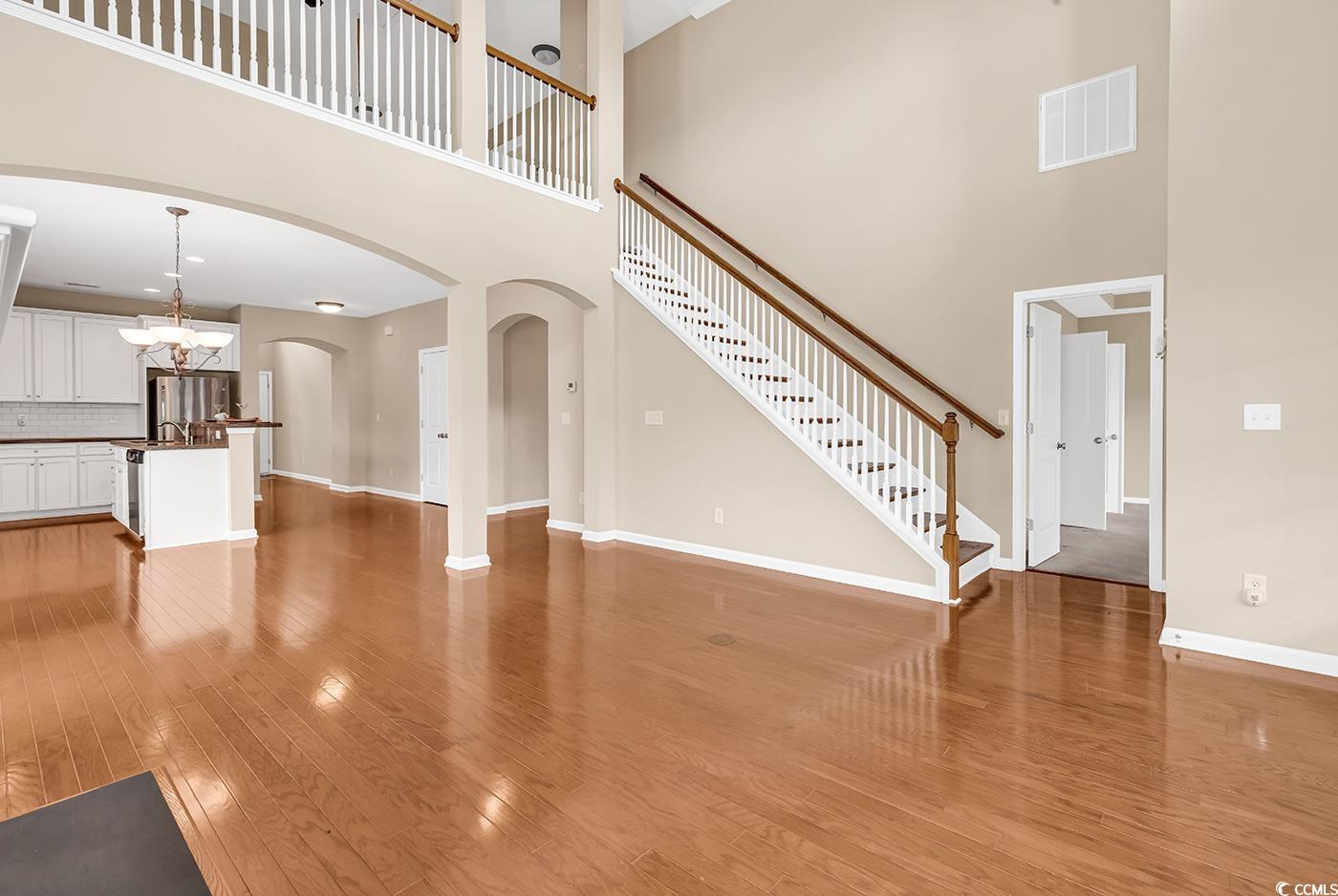 126 Dreamland Drive Murrells Inlet, SC 29576 - Photo 11 of 40 Unfurnished living room featuring a towering ceiling, light wood-style floors, baseboards, arched walkways, and stairs