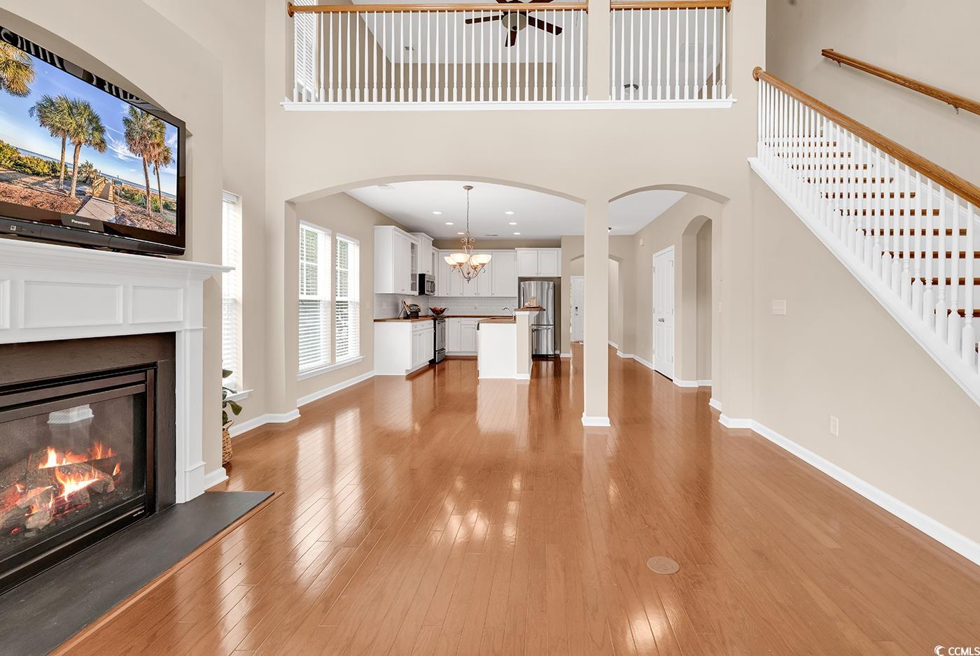 126 Dreamland Drive Murrells Inlet, SC 29576 - Photo 12 of 40 Unfurnished living room with a towering ceiling, a glass covered fireplace, light wood-style flooring, baseboards, and stairway