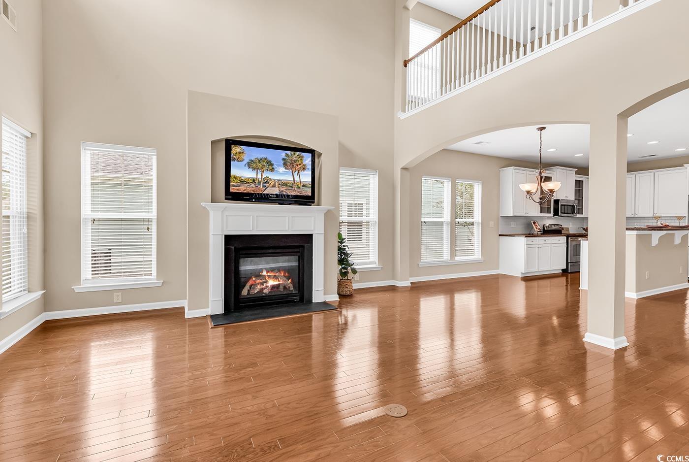 126 Dreamland Drive Murrells Inlet, SC 29576 - Photo 13 of 40 Unfurnished living room featuring a towering ceiling, a chandelier, wood finished floors, a glass covered fireplace, and baseboards
